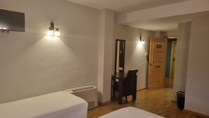 Habitación de hotel con dos camas individuales, un escritorio con silla, un espejo y una puerta con la etiqueta 