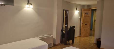 A hotel room with two single beds, a desk with a chair, a mirror, and a door labeled "i05".