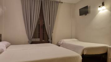 Habitación con dos camas, una ventana con cortinas, un televisor de pantalla plana y una lámpara fijada a la pared.