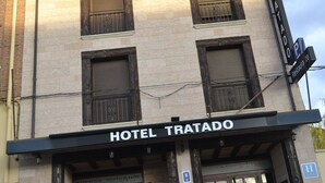 Ein Hotel namens "HOTEL TRATADO" mit einem Schild, einem Außenbereich mit Sitzgelegenheiten und einem sichtbaren Eingang.