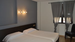 Ein Hotelzimmer mit zwei Betten, einem Nachttisch, einem Sessel, einem Fenster mit Vorhängen und Wandleuchten.