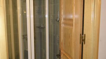 Un box de ducha con puerta de vidrio, una puerta de madera a la derecha y paredes con azulejos.