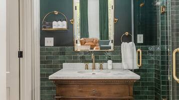 A bathroom with a dark green tiled wall, a wooden vanity with a mirror, and a glass shower enclosure.