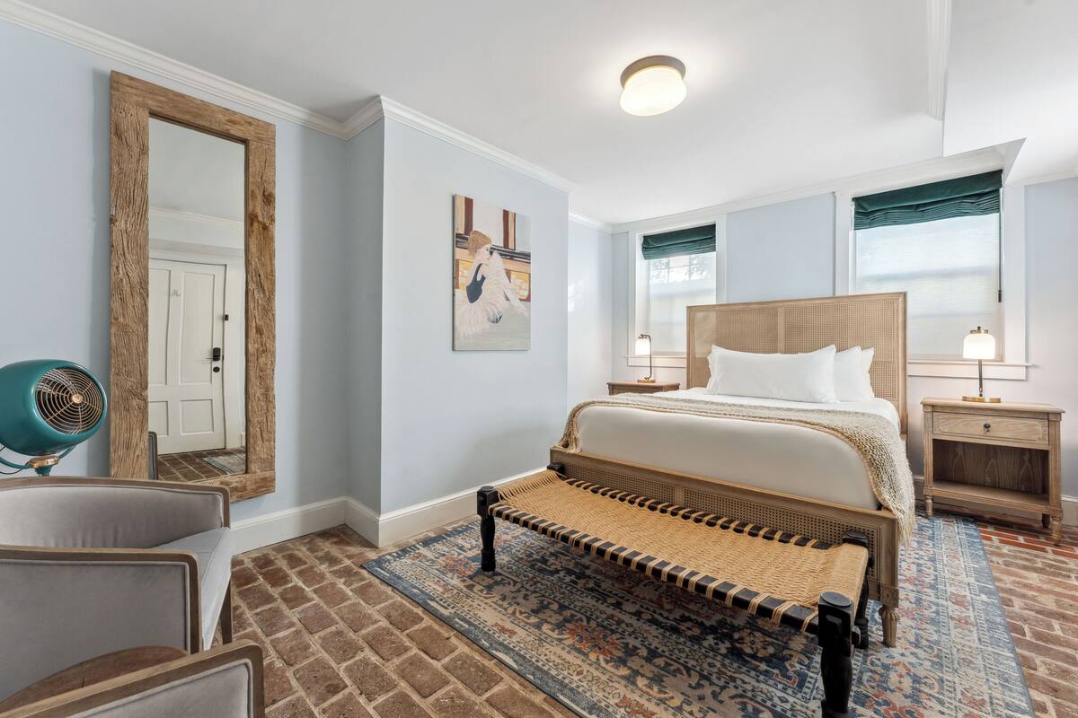 A bedroom with a large bed, a mirror, a chair, and a nightstand.