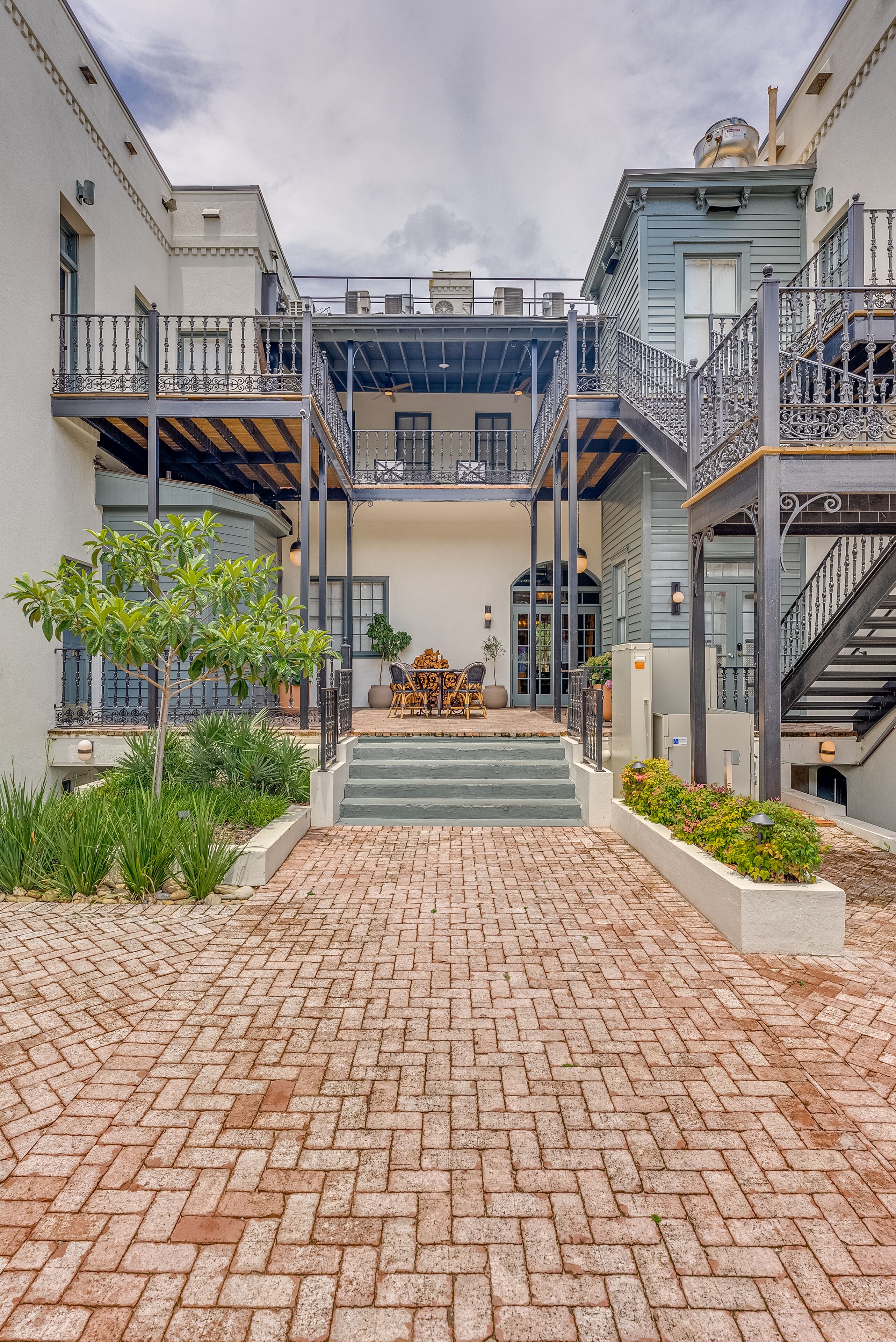 A courtyard with brick flooring, a central staircase, and a seating area with outdoor furniture.