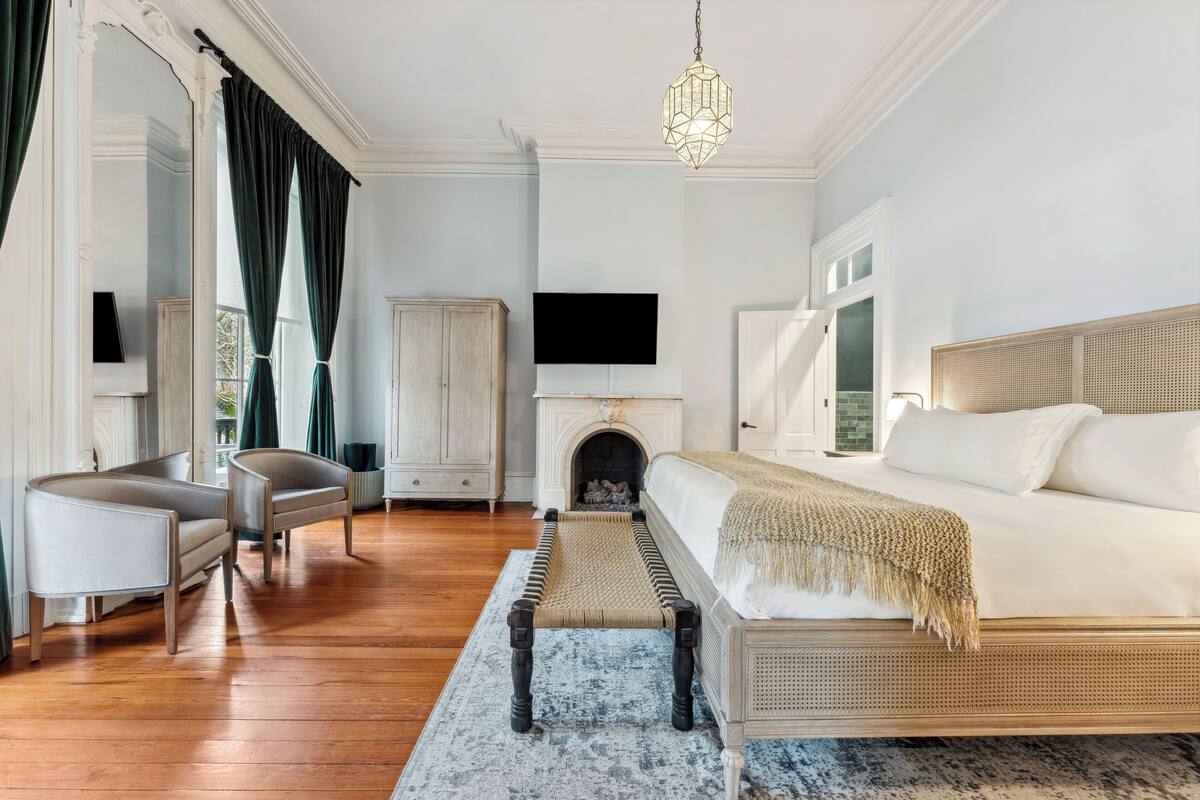 A bedroom with a large bed, a television above the fireplace, and a chandelier.