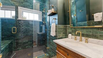 A bathroom with a glass-enclosed shower, a vanity with a sink, and a mirror.