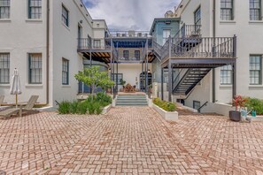 A courtyard with a brick floor, outdoor seating, and a central staircase leading to upper floors.
