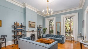 A spacious living room with a fireplace, a blue sofa, a leather ottoman, and a bookshelf. - Bellwether House (Savannah)