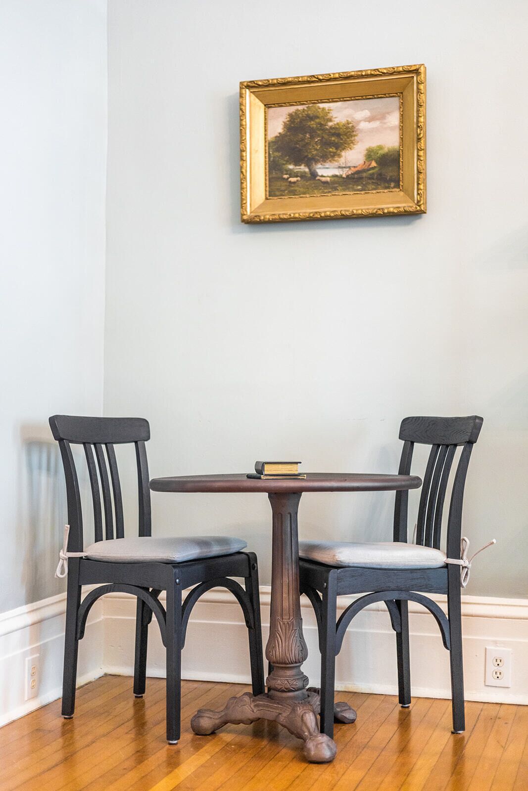 Een eettafel met twee stoelen, een lijst met een schilderij aan de muur en een houten vloer.
