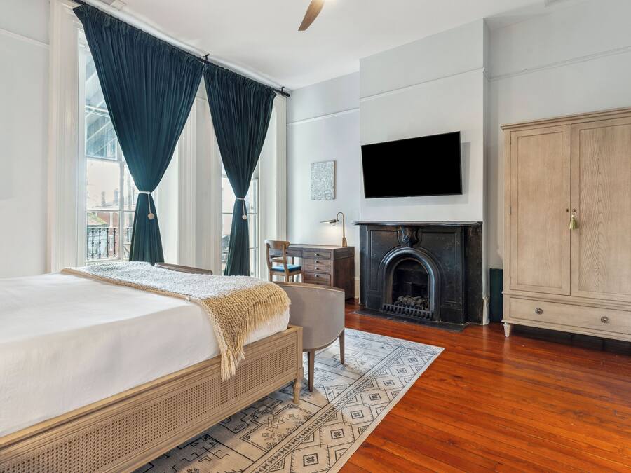 A bedroom with a bed, a desk, a chair, a television, a wardrobe, and a fireplace.