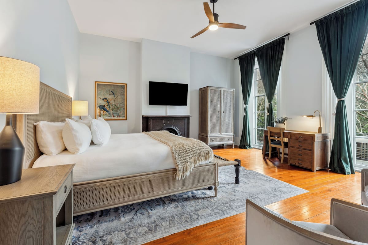 A spacious bedroom with a large bed, a desk, a wardrobe, and a television.
