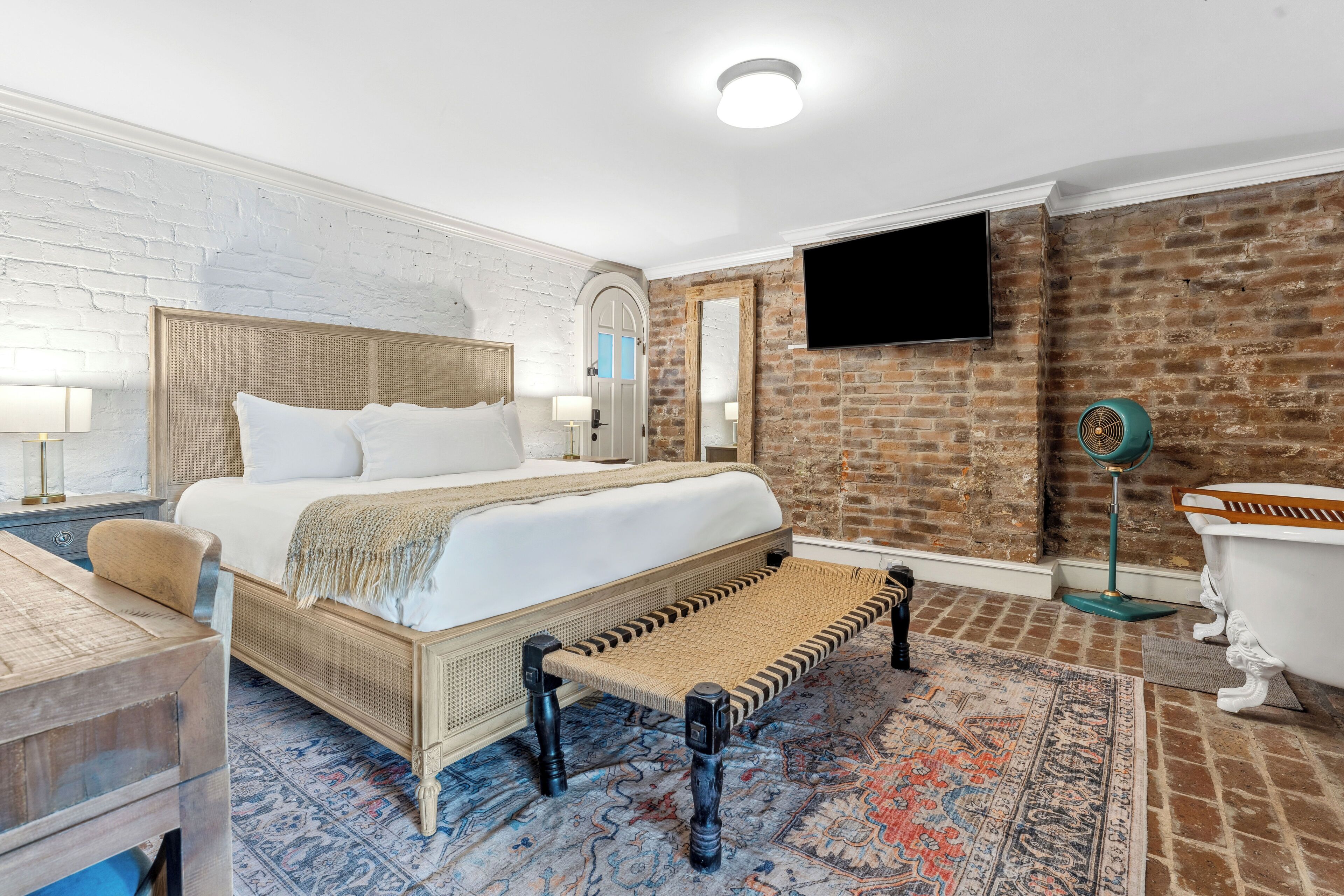 Una habitación de hotel moderna con una cama grande, una bañera clásica y una pared de ladrillo.