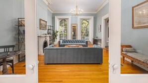 A spacious living room with a large blue sofa, a fireplace, and a chandelier. - Bellwether House (Savannah)