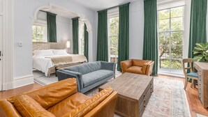 A spacious bedroom with a large bed, a sitting area with a sofa and armchairs, and a wooden coffee table. - Bellwether House (Savannah)