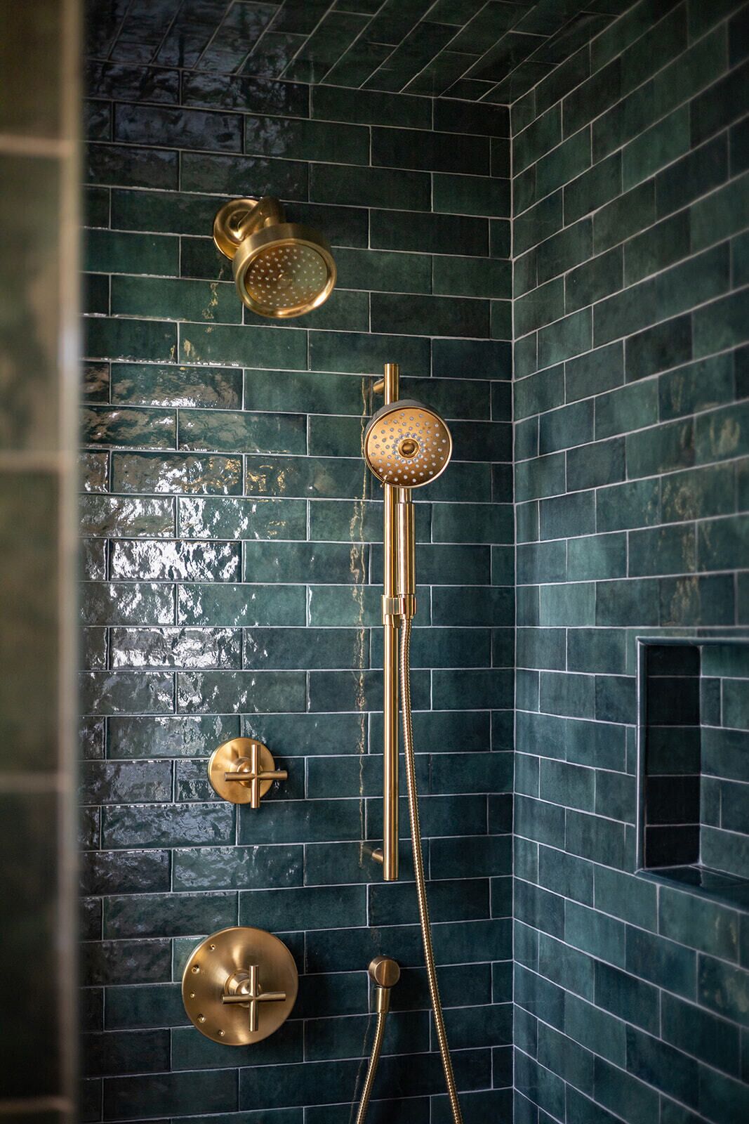 A bathroom with dark green tiled walls, a gold showerhead, and a gold faucet.