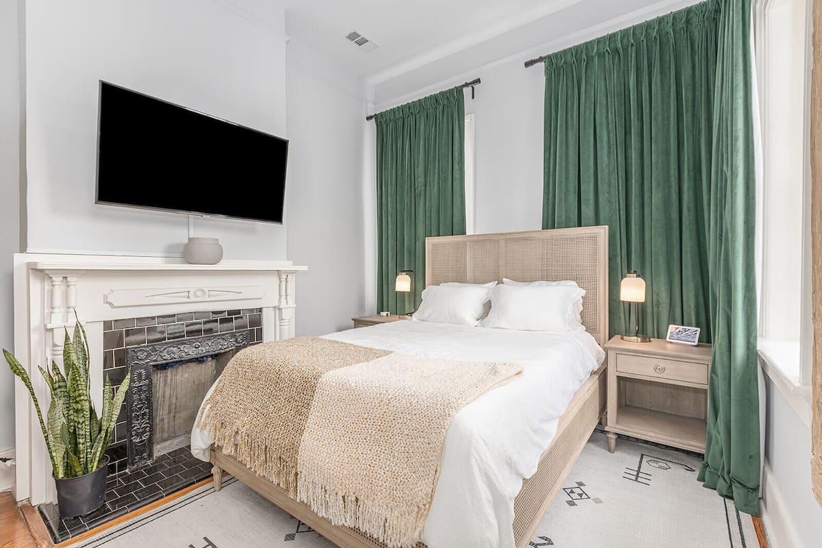 A modern bedroom with a bed, bedside tables, a TV, a fireplace, and green curtains.