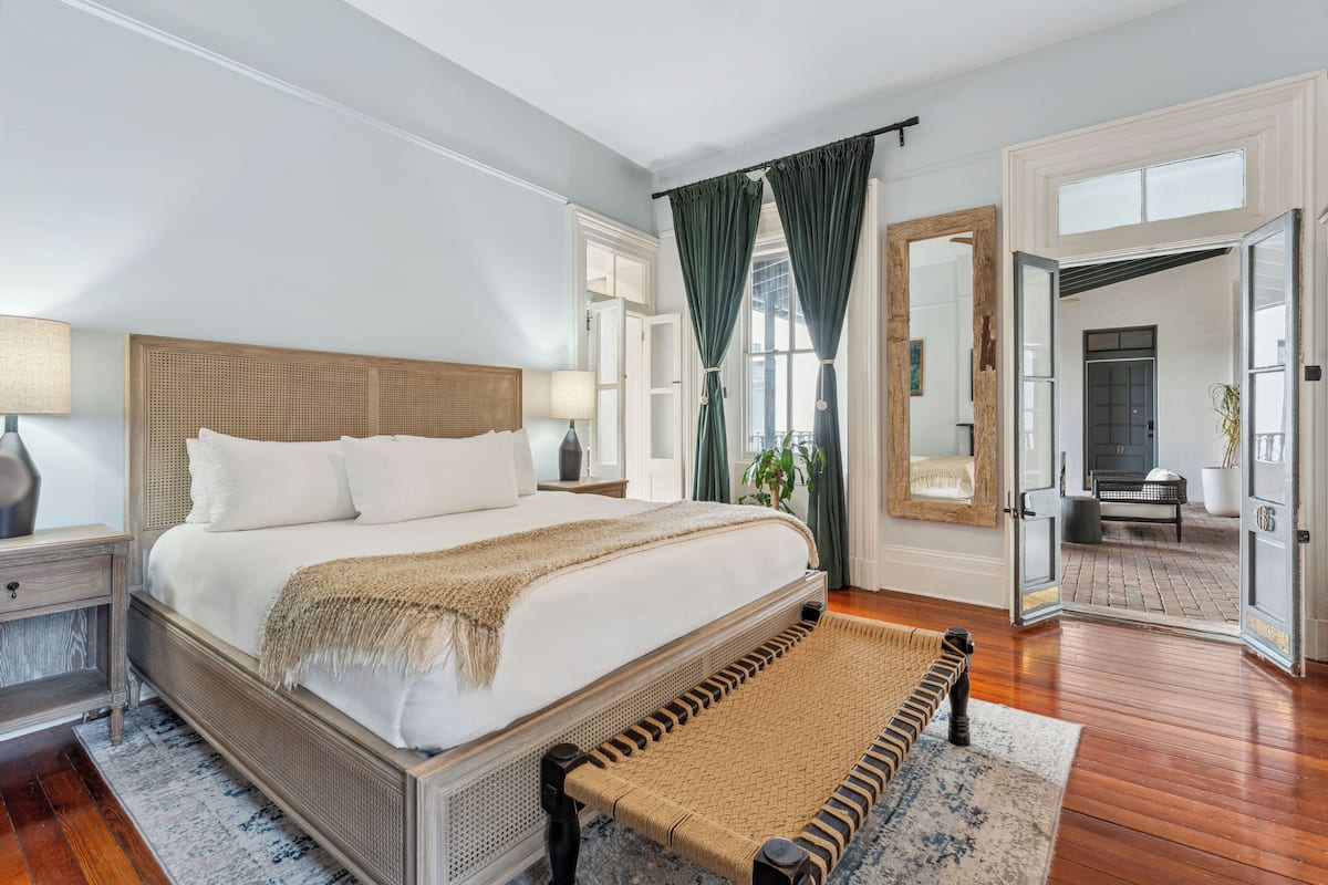 A spacious bedroom with a large bed, a wooden headboard, a bedside table with a lamp, and a woven bench.