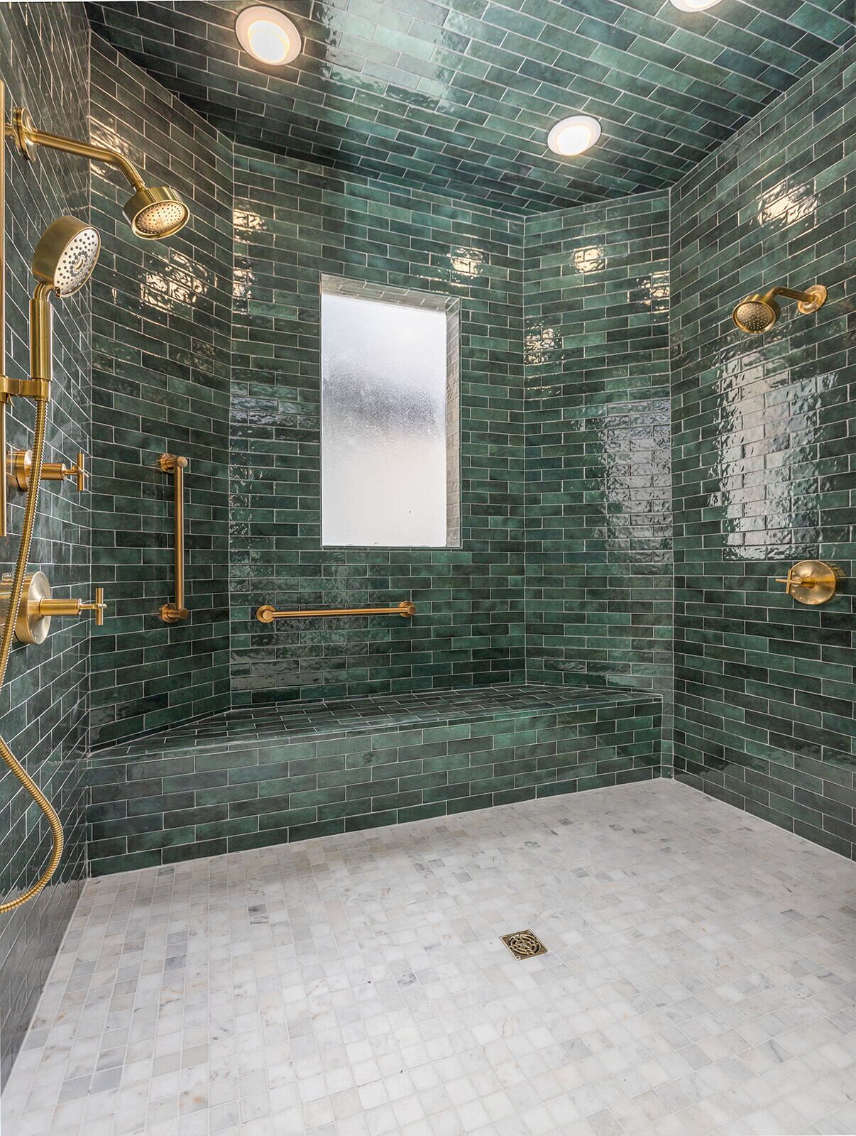 A bathroom with green mosaic tiles, a glass shower enclosure, and gold fixtures.
