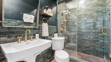 A bathroom with a white sink, gold fixtures, a toilet, and a glass-enclosed shower with a tiled wall.