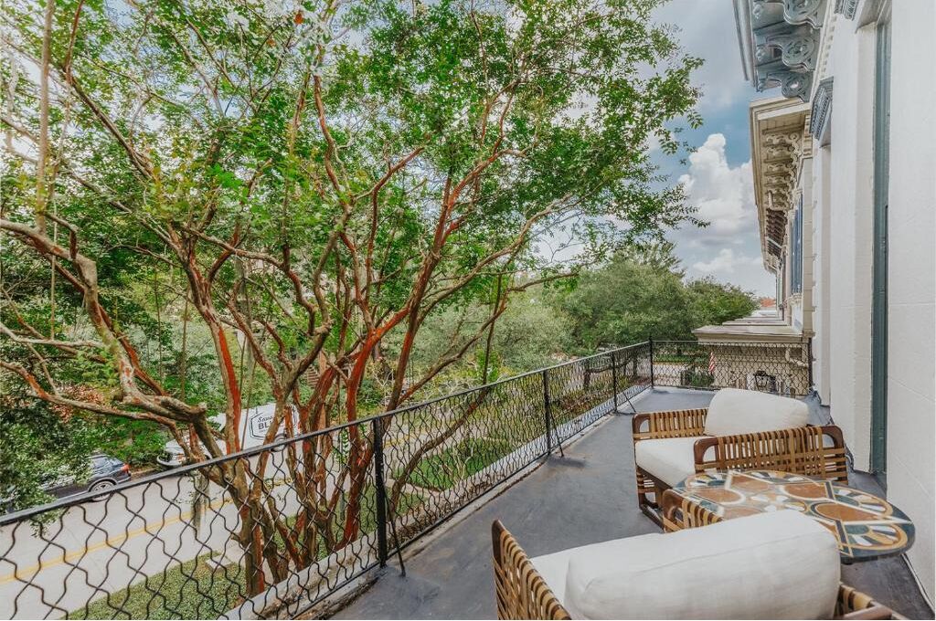 A balcony with wicker furniture, a view of trees, and a building with classical architecture.