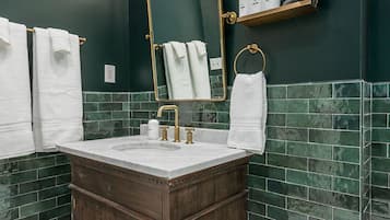 A bathroom with a dark green tiled wall, a wooden vanity with a white sink, and a mirror with a gold frame.
