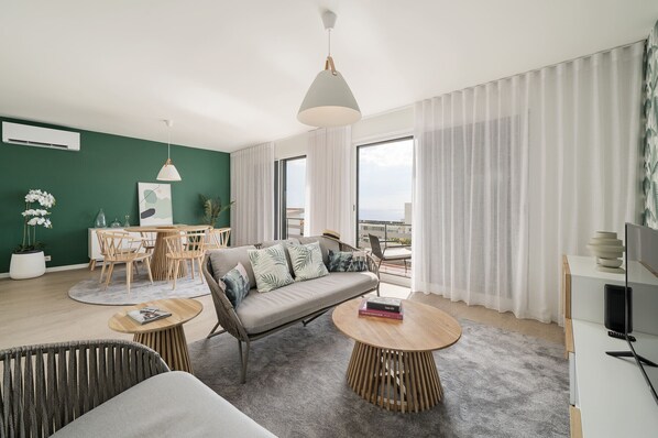 A modern living room with a sofa, two round tables, a dining table, and a view of the city.