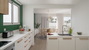 Una cocina moderna con armarios blancos, una estufa empotrada, una zona de comedor con mesa y sillas redondas, y un ventanal con cortinas.