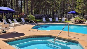 A pool area with lounge chairs and umbrellas, surrounded by a stone wall and trees.