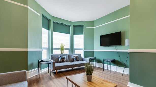 A modern living room with a grey sofa, wooden coffee table, and green walls. - Queen Street Apartments by Sasco (Blackpool)