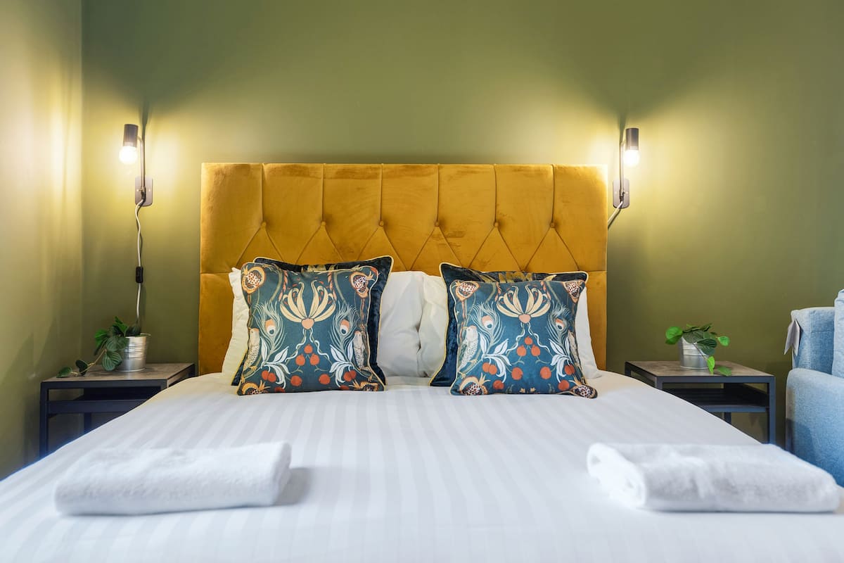 Een netjes opgemaakt bed met twee kussens, een hoofdbord en nachtkastjes met lampen.