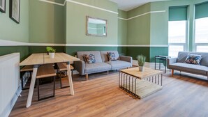 A modern living room with a green accent wall, a grey sofa, a wooden coffee table, and a dining table with benches. - Queen Street Apartments by Sasco (Blackpool)