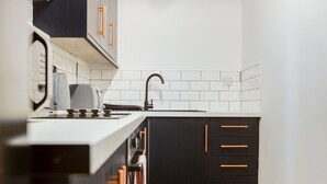 A modern kitchen with white tiled backsplash, black cabinets, and a stainless steel range hood. - Queen Street Apartments by Sasco (Blackpool)