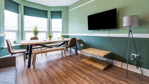 A modern room with a wooden dining table, chairs, a bench, a TV mounted on the wall, and a floor lamp. - Queen Street Apartments by Sasco (Blackpool)