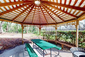 Relax in a serene outdoor setting surrounded by nature, with a picnic table and benches under a covered roof.