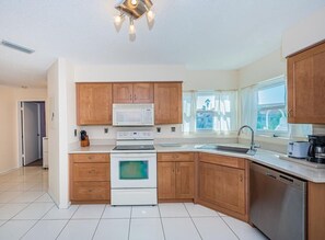 A modern kitchen with wooden cabinets, a microwave, an oven, a dishwasher, and a window providing natural light.
