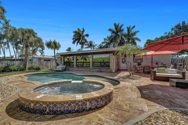 A backyard with a hot tub, a pool, and a covered patio area.