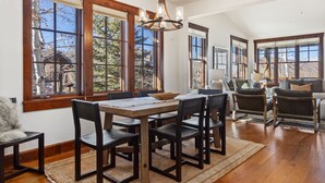 A spacious dining area with a wooden table and chairs, large windows with a view of trees and mountains, and a chandelier. - Outpost: Grand View 3230 - Air Conditioning! (Jackson)