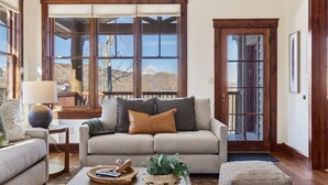 A living room with a sofa, a coffee table with a plant and a basket, and a window with a view of mountains. - Outpost: Grand View 3230 - Air Conditioning! (Jackson)