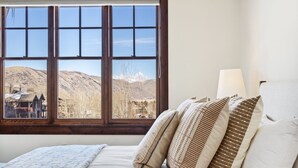A bedroom with a large window offering a mountain view, a bed with patterned pillows, and a bedside lamp. - Outpost: Grand View 3230 - Air Conditioning! (Jackson)
