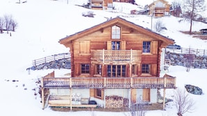 Eine Holzhütte mit Balkon, Steinmauer und Schneebedeckung.