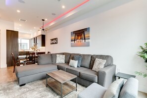Una sala de estar moderna con un sofá seccional gris, una mesa de centro de madera, y un comedor con una mesa y sillas de madera.