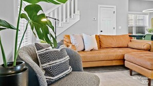 Een moderne woonkamer met een hoekbank, een potplant en een trap.