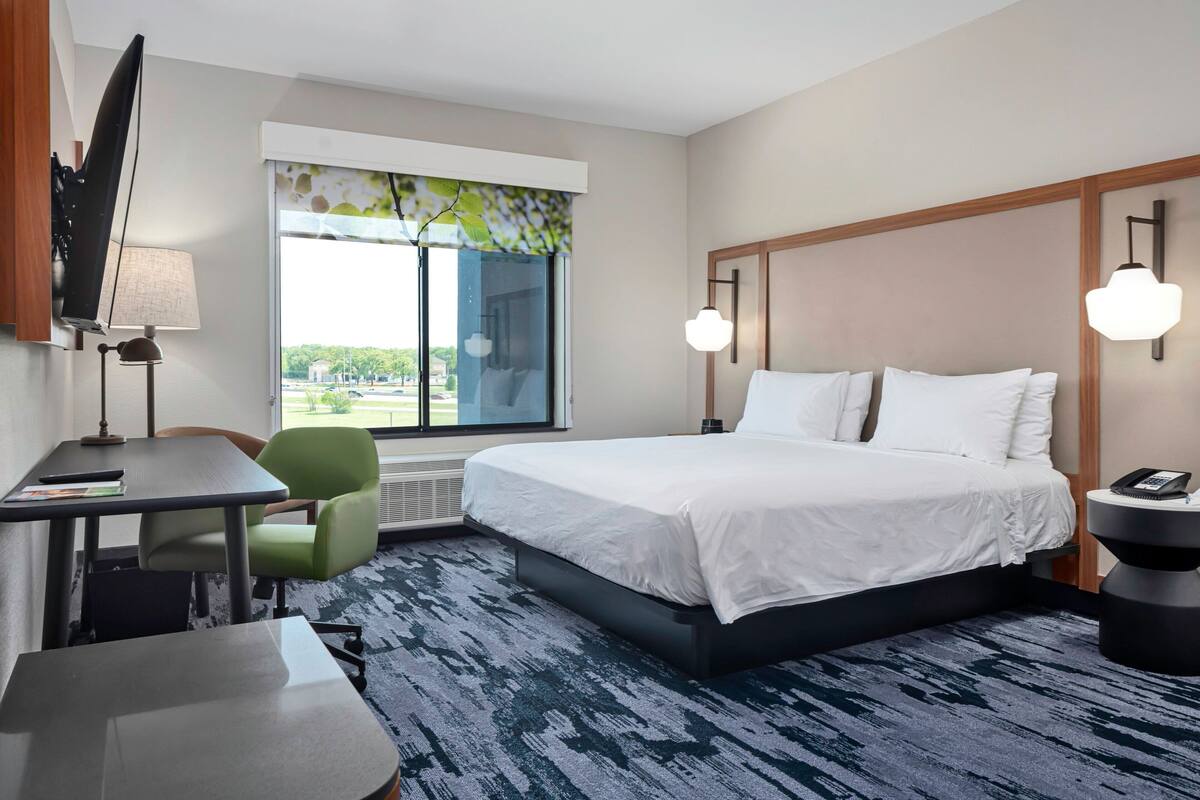 Une chambre d’hôtel avec un lit, un bureau, une chaise, une télévision et une fenêtre donnant sur un paysage agréable.