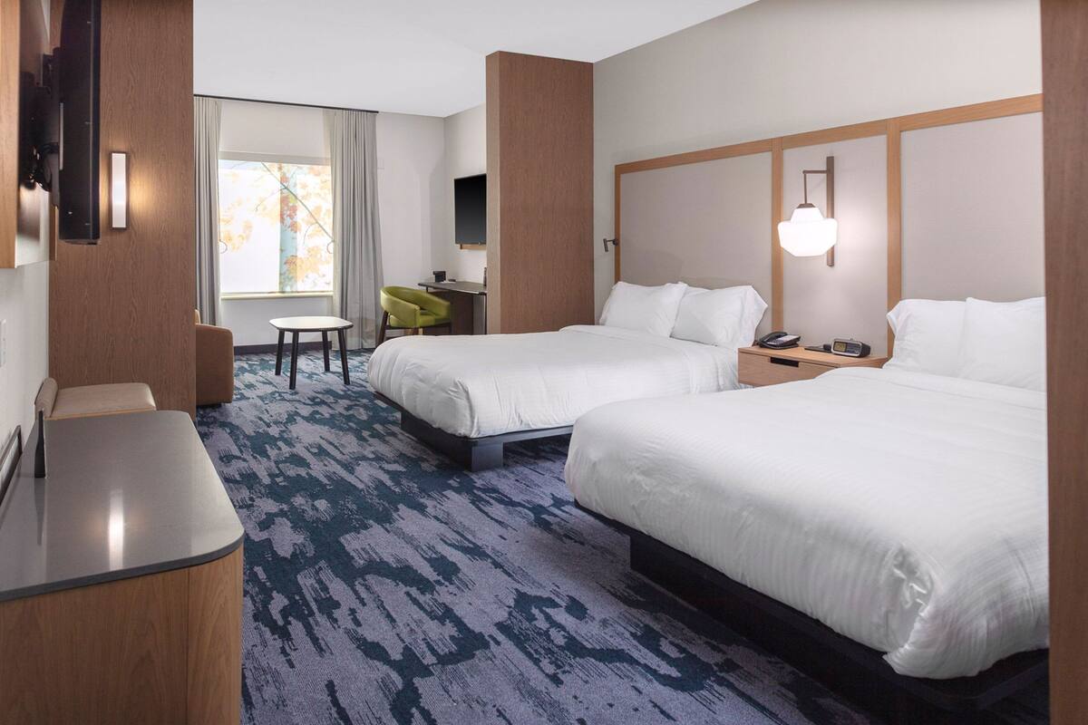 Une chambre d’hôtel avec deux lits, un bureau, une chaise et un téléviseur.