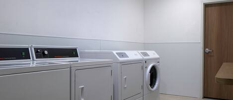 A laundry room with three stacked washers and dryers, a wooden door, and a light-colored tiled floor.