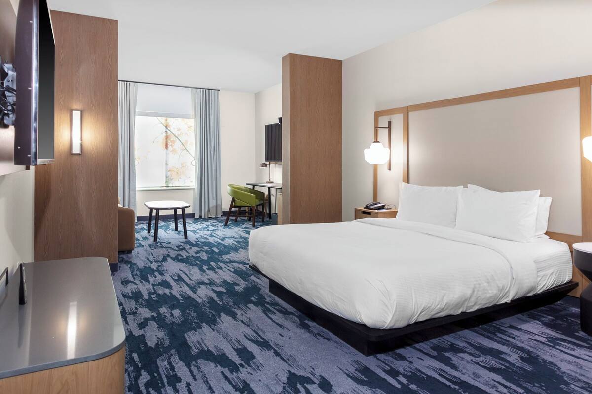 Une chambre d’hôtel avec un grand lit, un bureau, une chaise, une télévision et une fenêtre avec des rideaux.