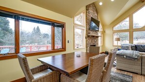 Un comedor acogedor con chimenea de piedra, sillas de mimbre y ventanas amplias con vistas a árboles.