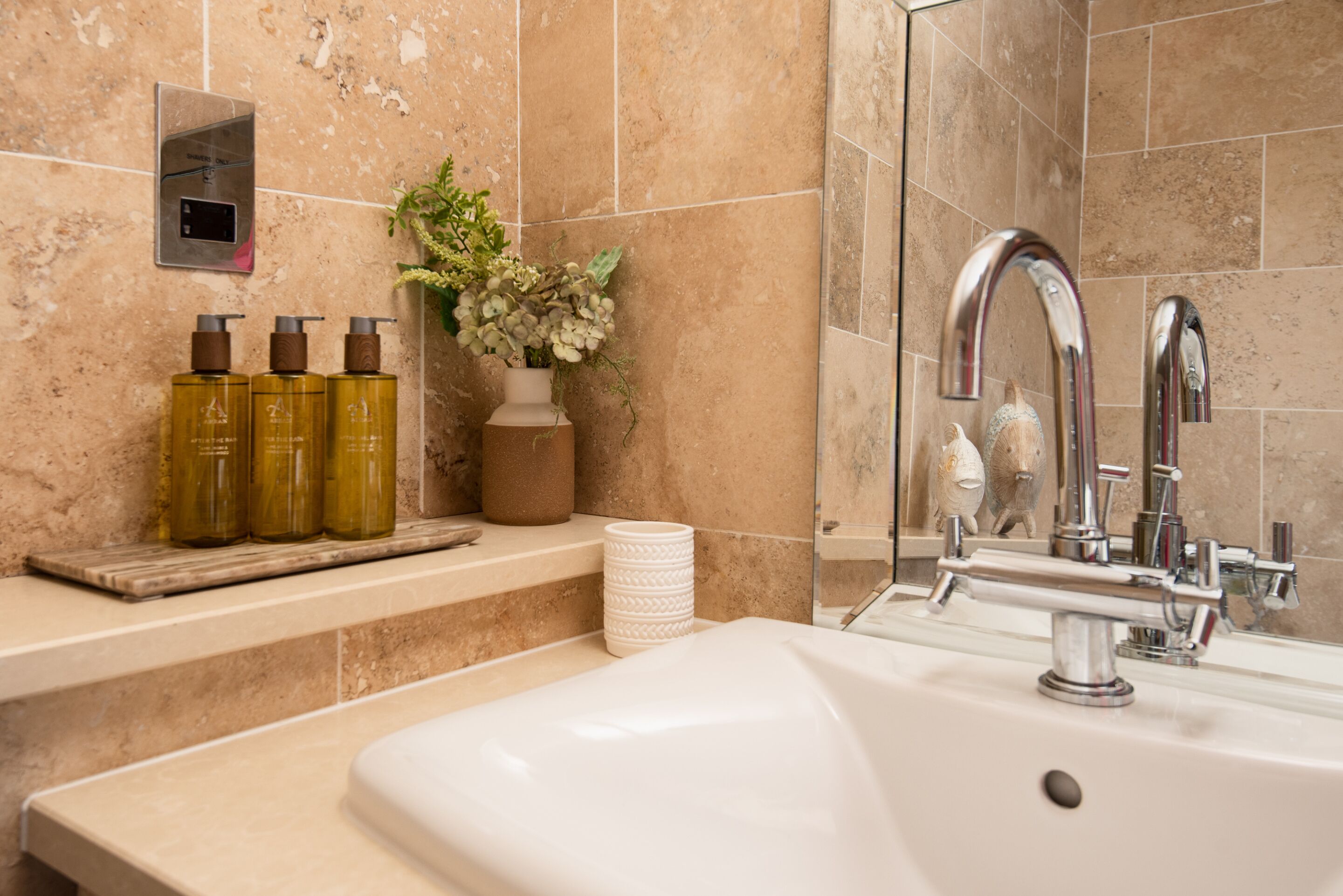 Un baño con lavabo, espejo, ducha y artículos de aseo en un estante.