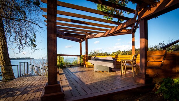 A wooden deck with a grill and seating area overlooking a body of water. - Ocean Tide (Unit A+B) - Waterfront Condo - Sleeps 6 - Pool - Family (Nanoose Bay)